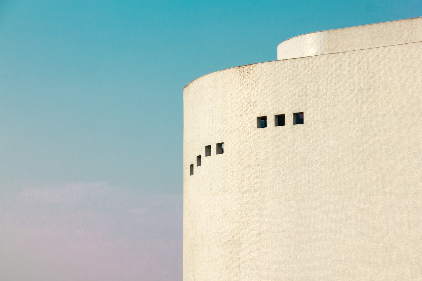 Pale sculptural building volume against a soft blue sky.